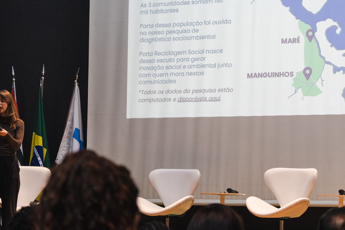 Apresentação do Porto Reciclagem Social no palco do II Fórum, com o mapa de Manguinhos, Maré e Colônia Z-10 no telão.